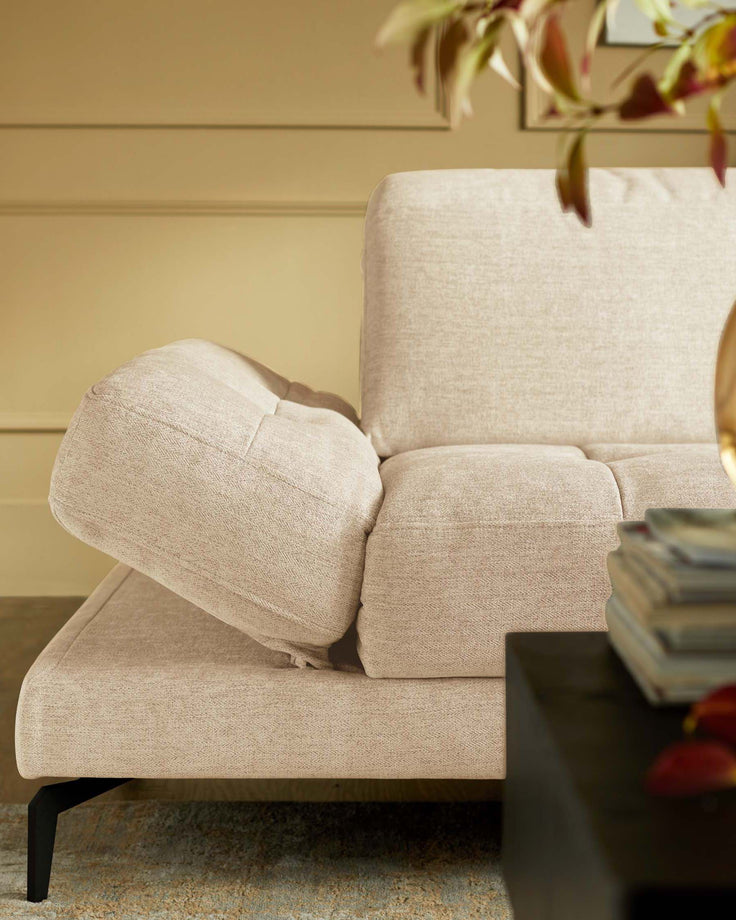 A close-up of a stylish, light-beige sofa with an adjustable headrest, and a dark wooden side table.