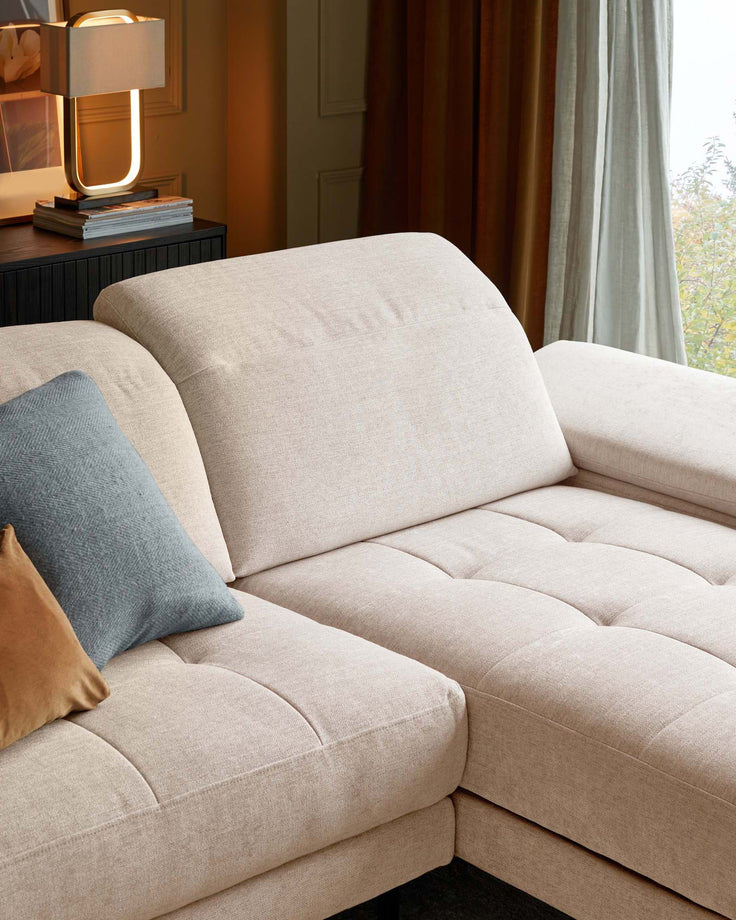 A modular sofa in a light beige fabric, with a blue and brown cushion on the left side.