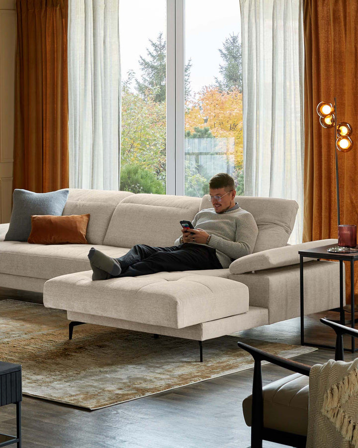A modern living room with a large beige sofa, stylish side table, floor lamp, and elegant armchair.