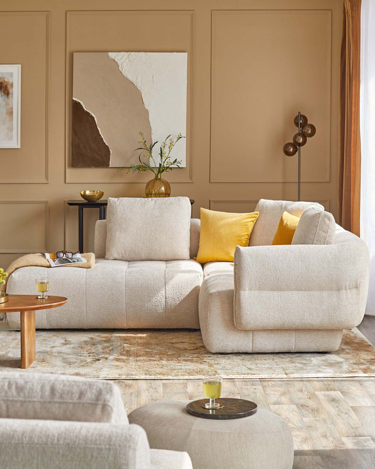 Cozy beige sectional sofa with yellow accent pillows, round wooden side table, and soft textured ottoman in a warm, inviting space.