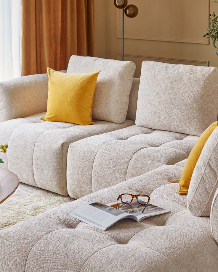 Cozy, modern beige sectional sofa with plush cushions, complemented by a yellow velvet throw pillow and a wooden coffee table.
