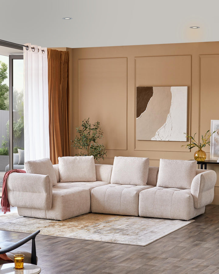 A modern, beige sectional sofa with plush cushions and armrests, paired with a textured rug and stylish decor elements.