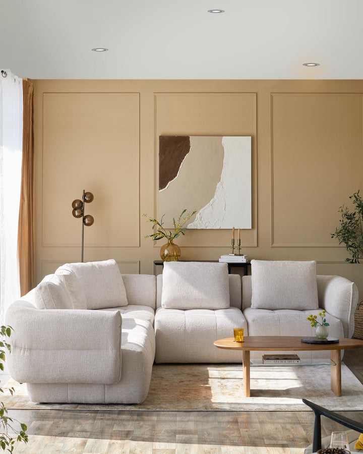 Cozy light gray sectional sofa, wooden coffee table, and stylish floor lamp against a warm-toned wall with abstract art.