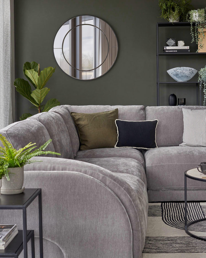 Luxurious gray sectional sofa with colorful pillows, round mirror, modern shelves, potted plant, and stylish coffee table.