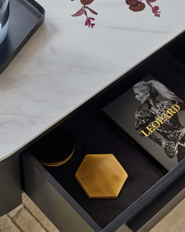A stylish open drawer showing a book and gold coasters on a marble-topped table.