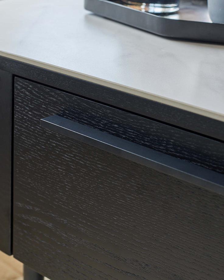 Close-up of a black, wood-grain drawer with a sleek, metal handle, set beneath a light, marble-effect top surface.