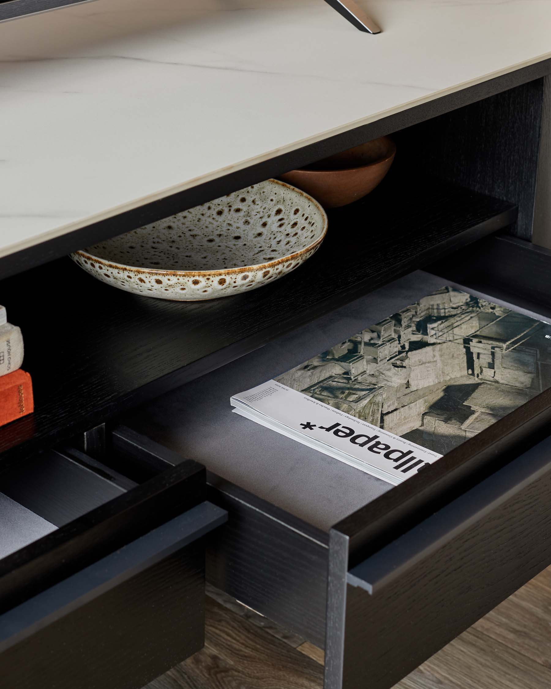 A contemporary dark wood cabinet with drawers open, revealing stylish storage with bowls and a magazine.