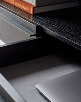 A stylish, open drawer desk with a black wood grain finish and a laptop inside. Perfect for a modern office space.