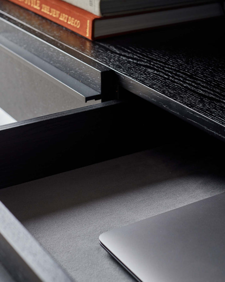 A stylish, open drawer desk with a black wood grain finish and a laptop inside. Perfect for a modern office space.