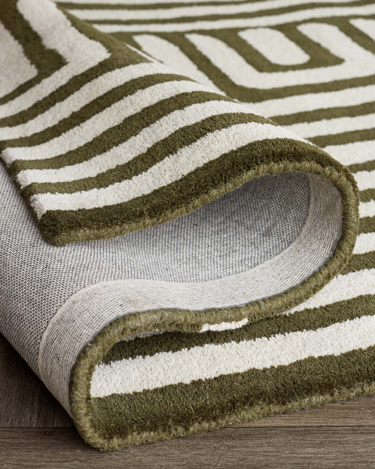 A patterned rug with green and white stripes is partially rolled up on a wooden floor. The rug has a distinct border.
