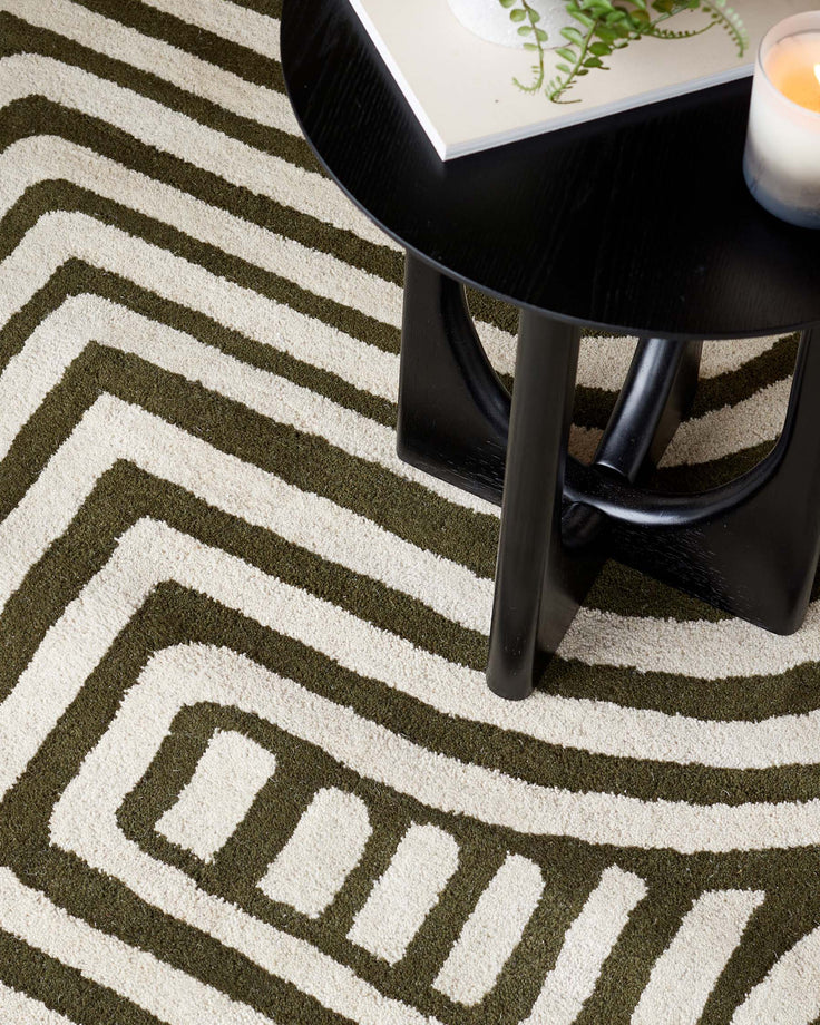 A close-up shows a round, black table with curved legs, sitting on a green and white striped rug, alongside books and a candle.