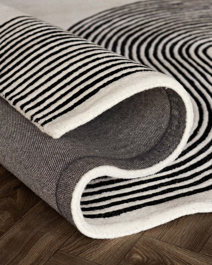 Rolled black and white striped rug on a wooden floor, showcasing a modern, minimalist design.