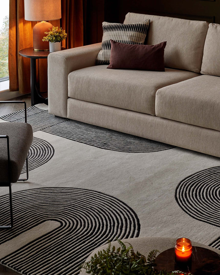 Stylish living room scene with sofa, accent pillows, patterned rug, side table, lamp, chair and decorative accessories.