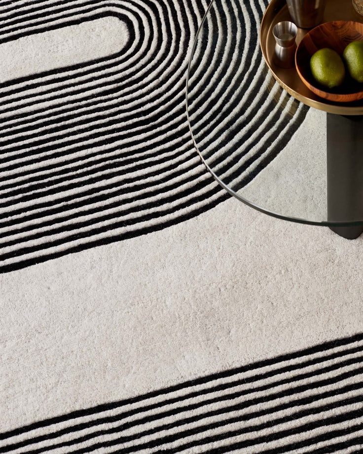 A glass-topped coffee table sits upon a monochrome rug with black, linear and curved designs.