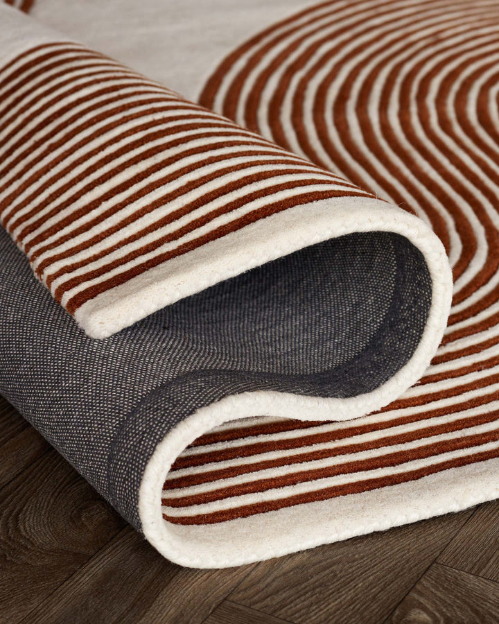 A rolled-up rug with brown and cream stripes and a textured grey underside sits on a dark wooden floor.