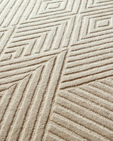Beige carpet with geometric design, creating a textured, abstract pattern. Neutral tones for a modern living space.