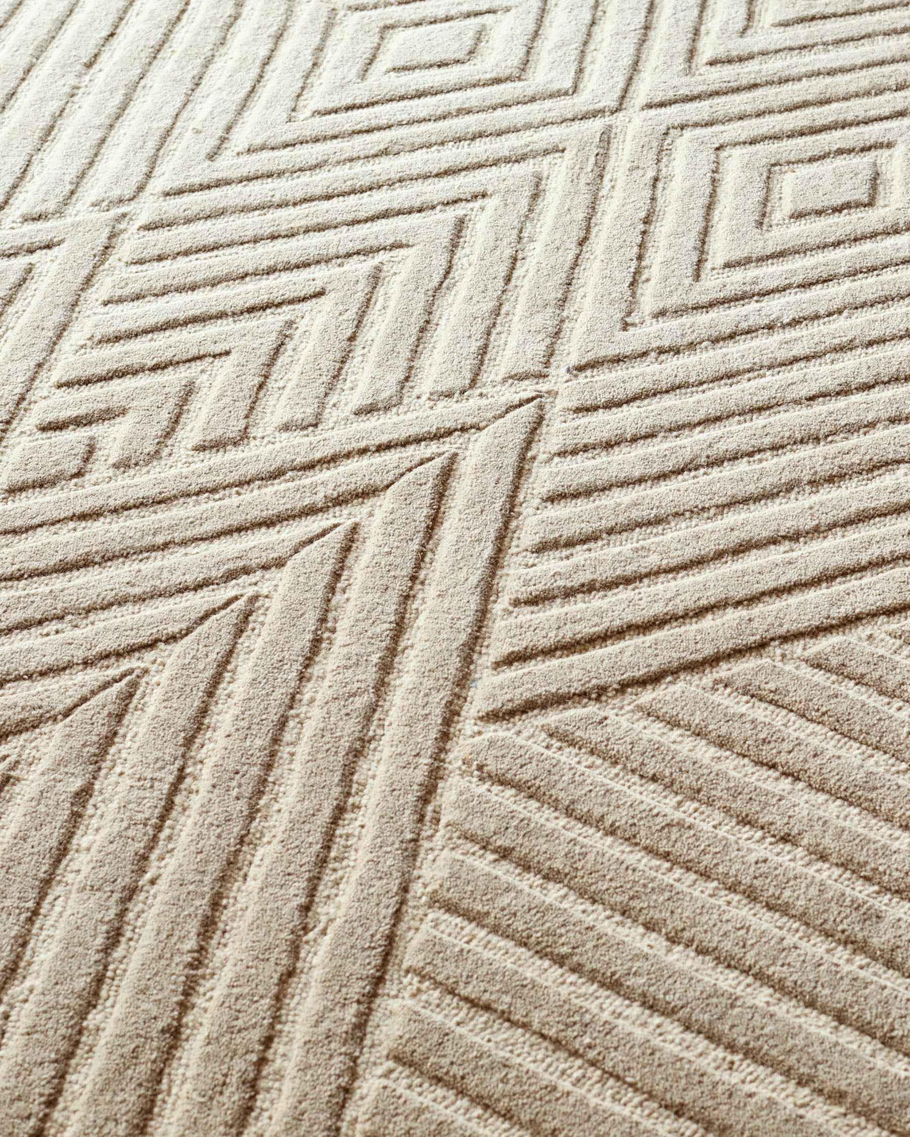 Beige carpet with geometric design, creating a textured, abstract pattern. Neutral tones for a modern living space.