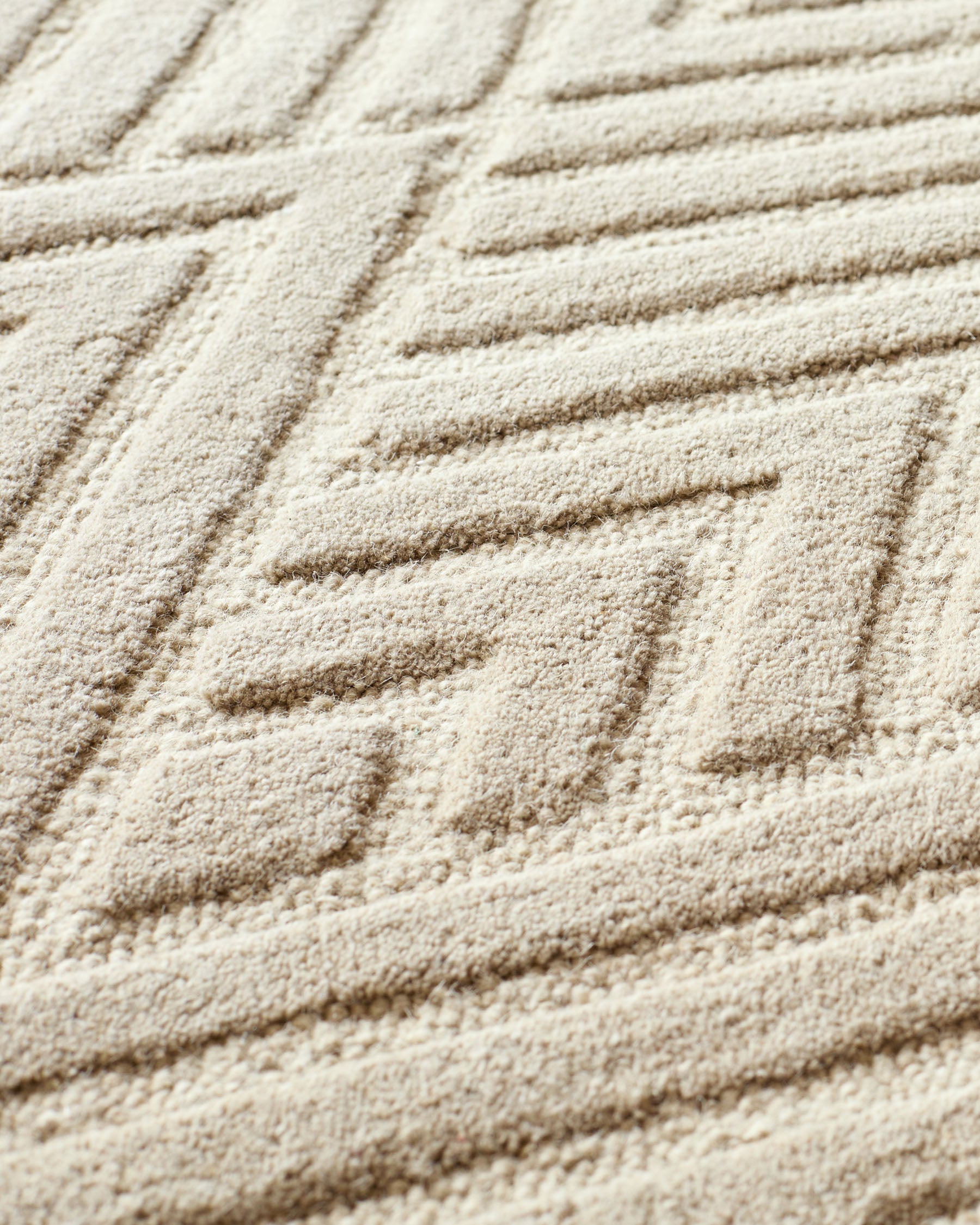 Close-up of a cream carpet with a geometric pattern. The textured surface is soft and plush, ideal for a cosy living space.