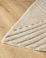 Close-up of a textured beige rug on a wooden floor. The rug features a striped and dotted pattern.