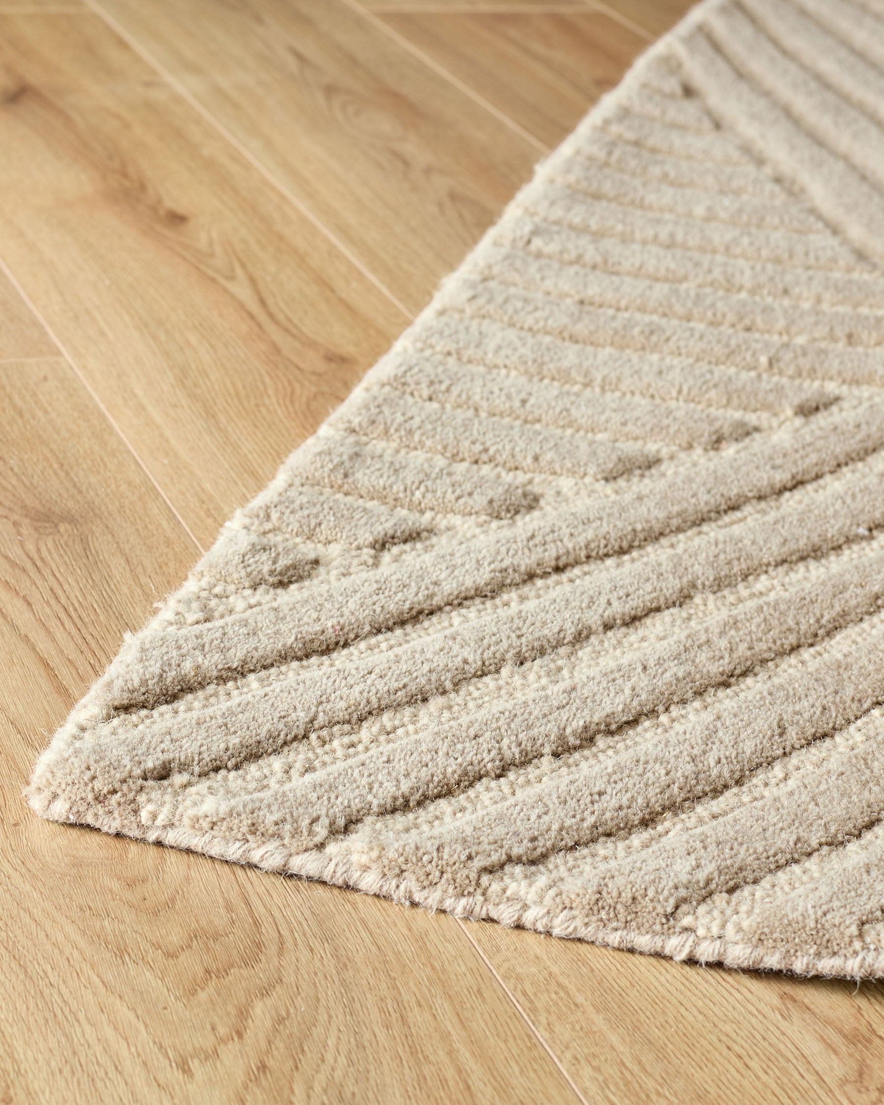 Close-up of a textured beige rug on a wooden floor. The rug features a striped and dotted pattern.