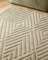 Close up shot of a textured, beige rug with geometric diamond pattern. A small section of a green sofa is also visible.