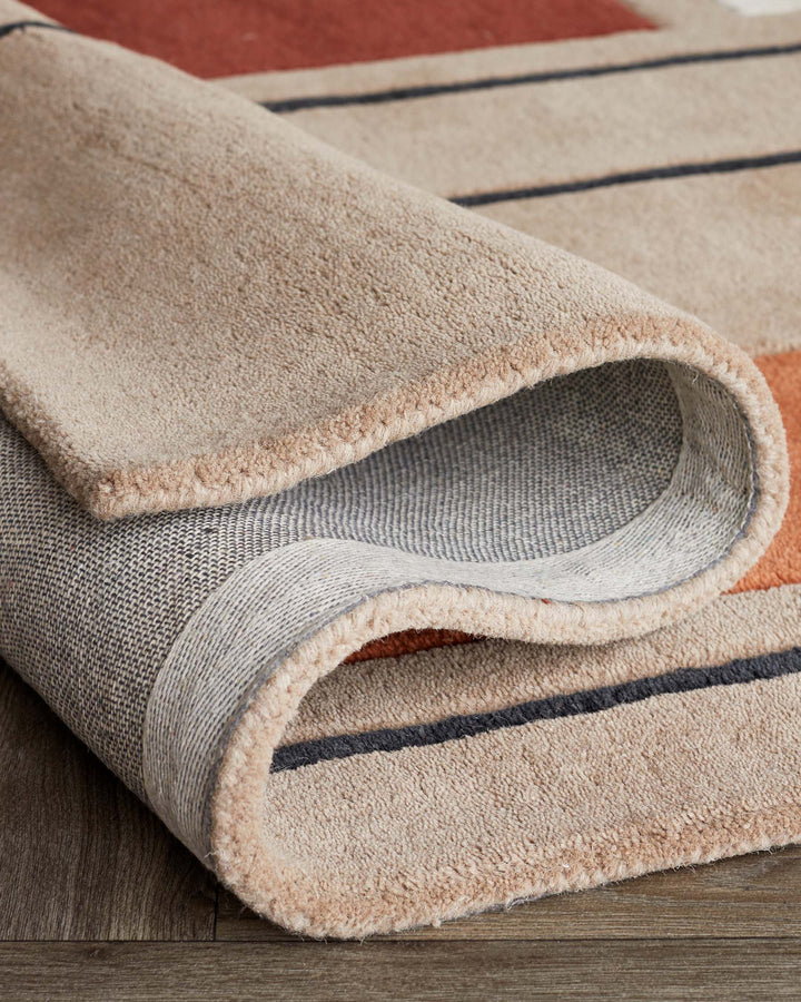A rolled-up rug with a textured beige surface, geometric design and a grey backing, displaying its quality and craftsmanship.