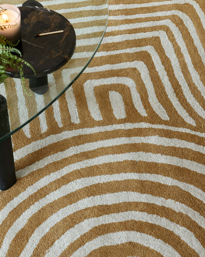 Abstract patterned rug with marble side table featuring glass top and black legs, beside a lit candle.