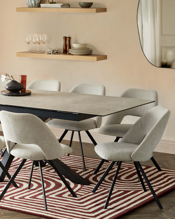 Dining table and chairs with a modern design, sitting on a red and white patterned rug. A shelf with decorations is in the background.
