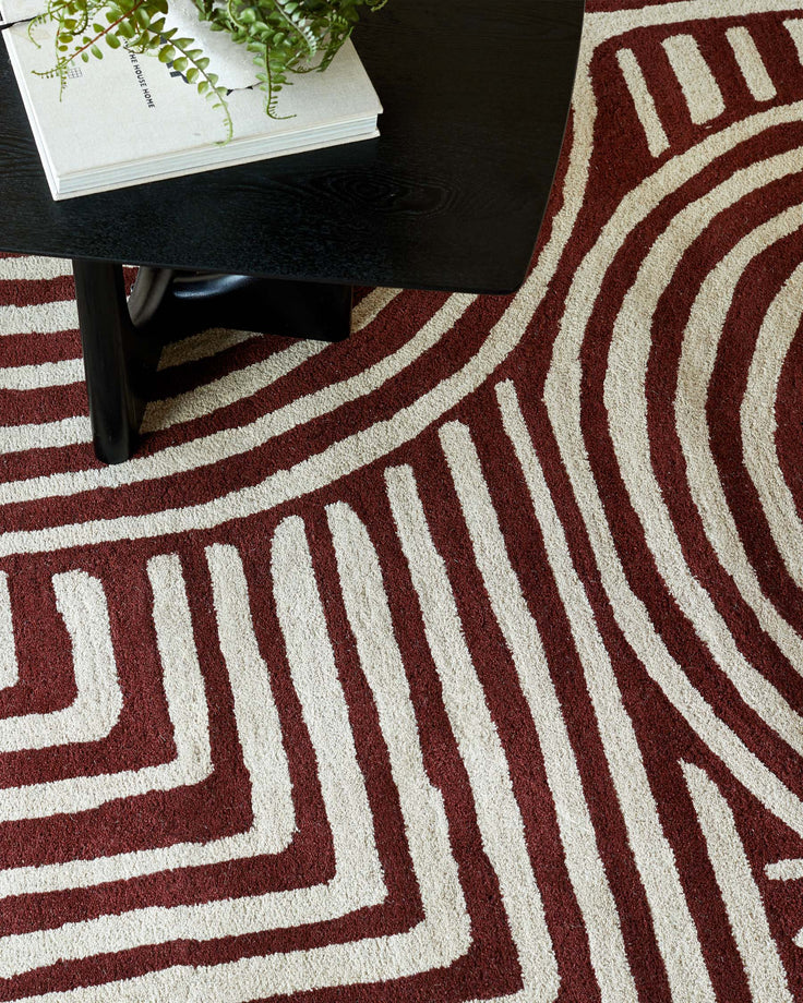Stylish black coffee table with a book and plant on top, placed on a patterned red and cream rug.