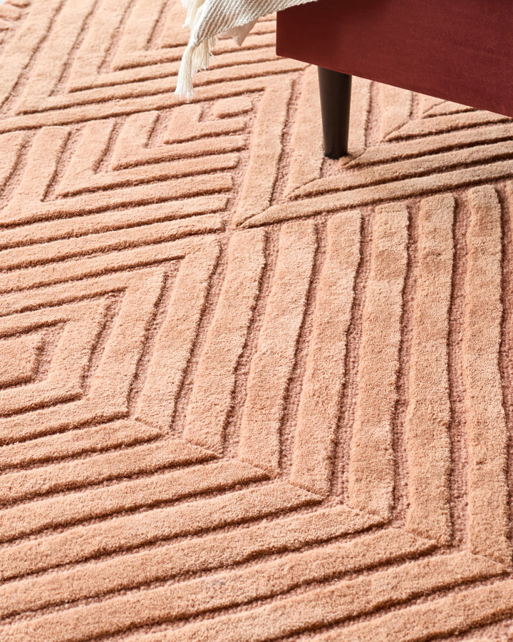 Close-up of a patterned rug under a portion of a sofa or chair, showcasing a textured surface and warm colour palette.