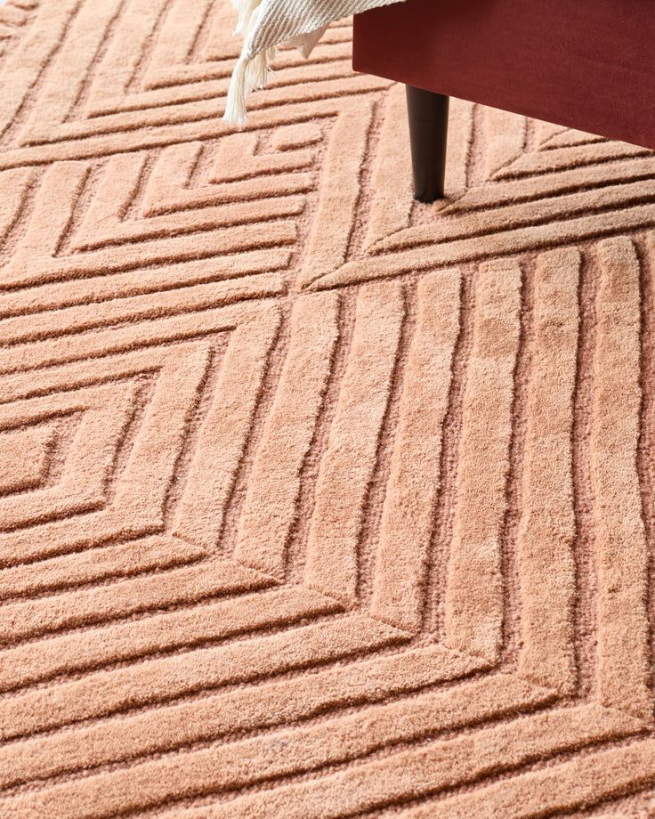 Close-up of a patterned rug under a portion of a sofa or chair, showcasing a textured surface and warm colour palette.
