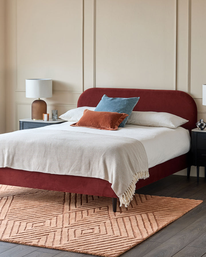 A stylish red velvet bed with matching rug and bedside tables creates a warm and inviting bedroom space.