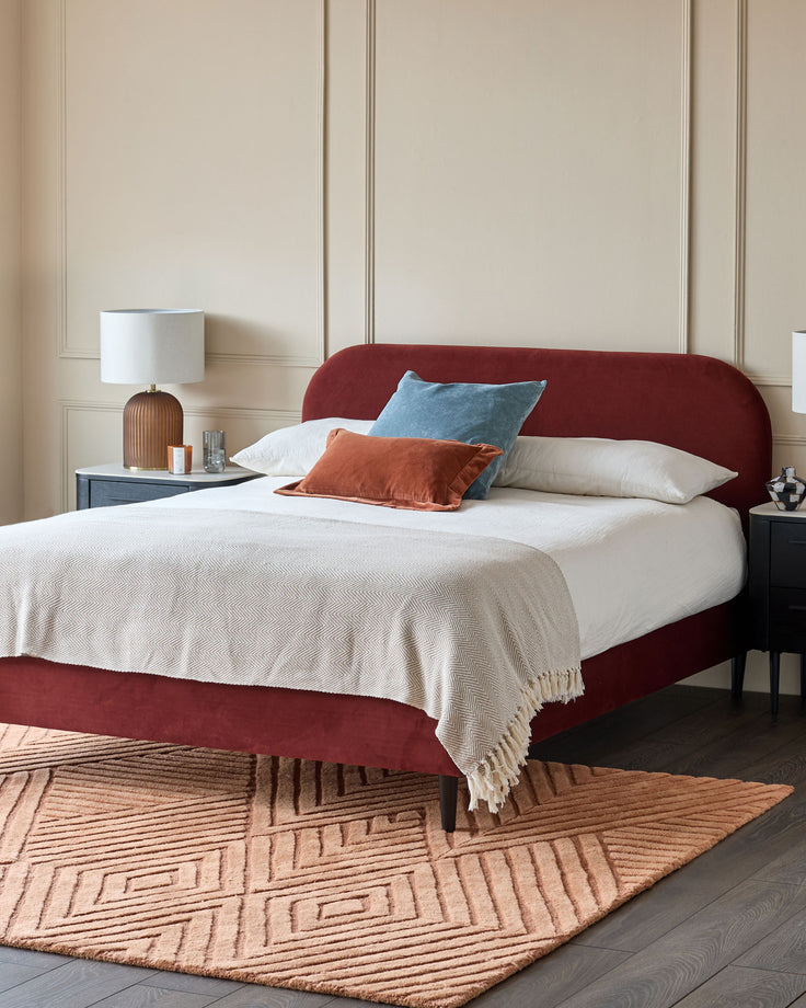 A stylish red velvet bed with matching rug and bedside tables creates a warm and inviting bedroom space.