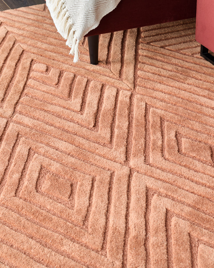 A textured, geometric-patterned rug, with a maroon chair and throw partially visible.