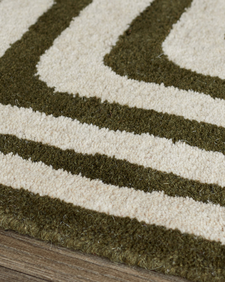 Close-up of dark green and cream wool rug with abstract diagonal stripe pattern and sculpted texture on wooden floor.