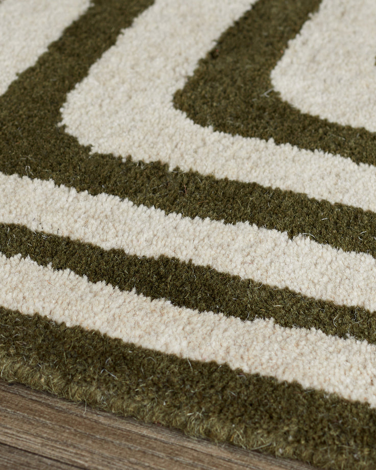 Close-up of dark green and cream wool rug with abstract diagonal stripe pattern and sculpted texture on wooden floor.