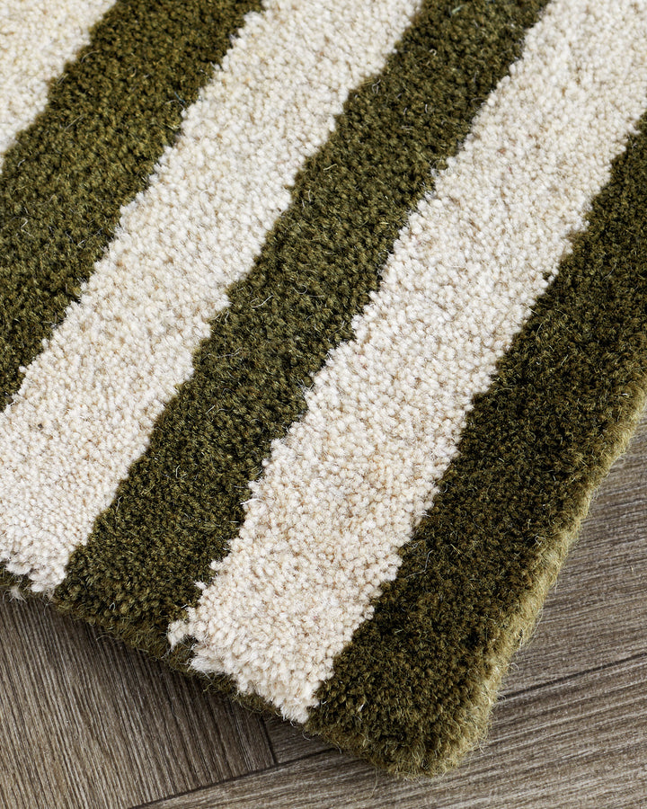 Close-up of dark green and cream striped wool rug on gray wood flooring, showing textured surface detail.