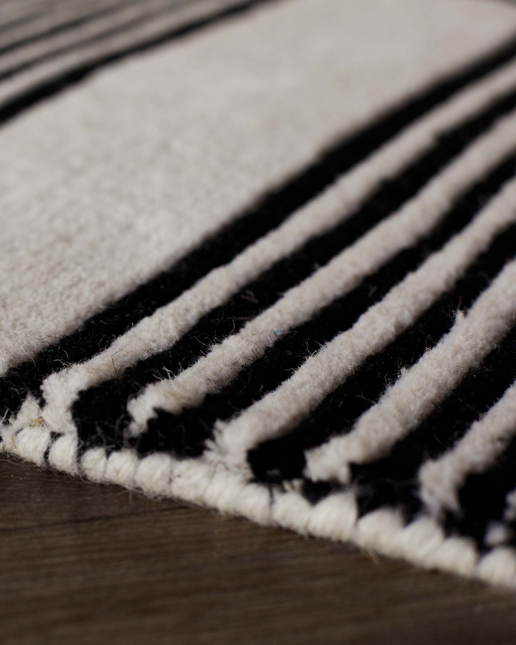 Close-up of black and cream striped wool rug with textured, sculpted surface and finished edge detail.