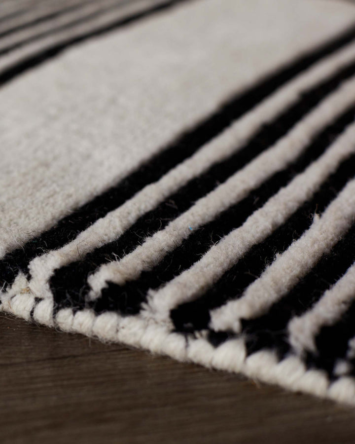 Close-up of black and cream striped wool rug with textured, sculpted surface and finished edge detail.