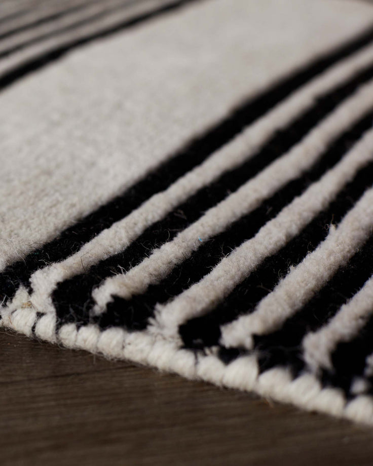 Close-up of black and cream striped wool rug with textured, sculpted surface and finished edge detail.