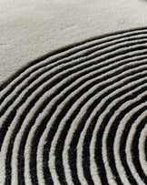 Close-up of sculpted wool rug with curved monochrome striped pattern in cream and charcoal tones.