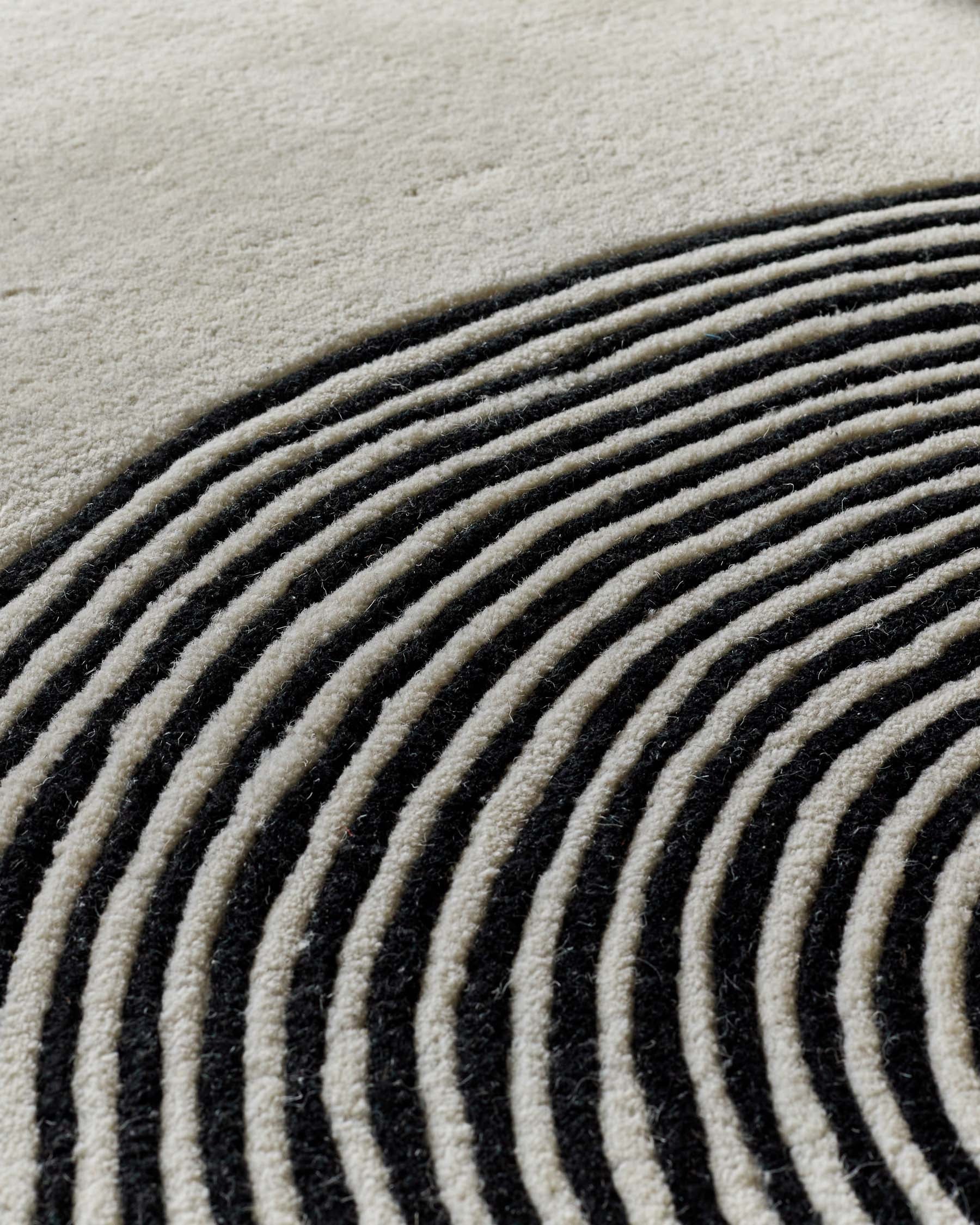 Close-up of sculpted wool rug with curved monochrome striped pattern in cream and charcoal tones.