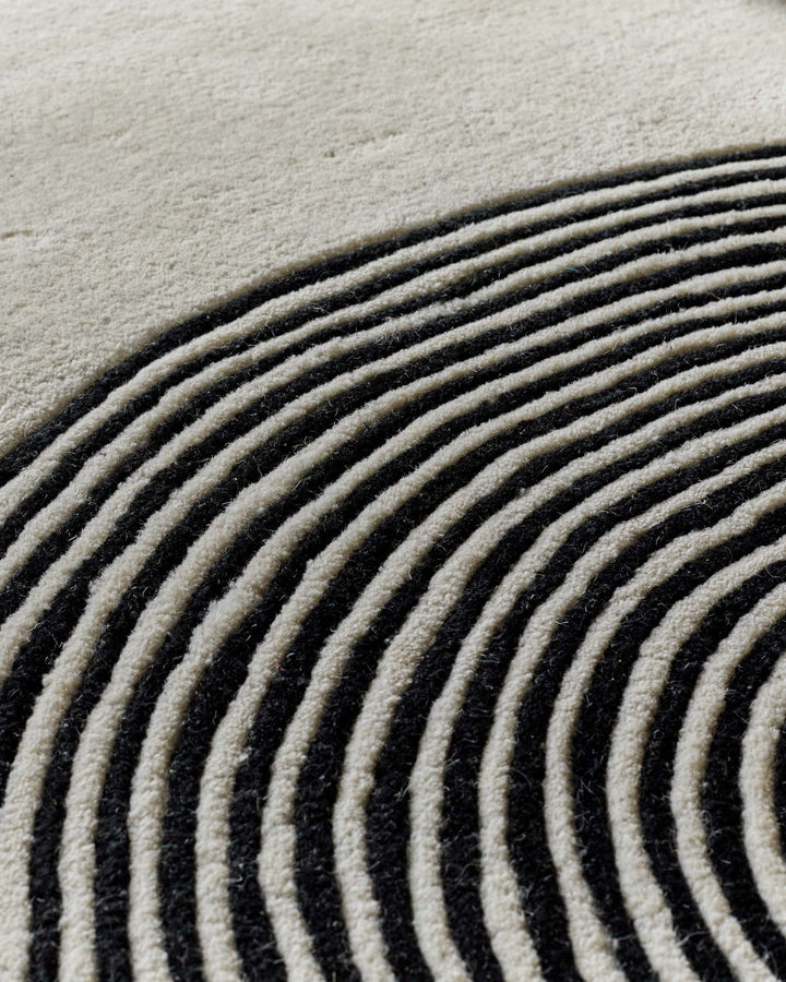Close-up of sculpted wool rug with curved monochrome striped pattern in cream and charcoal tones.
