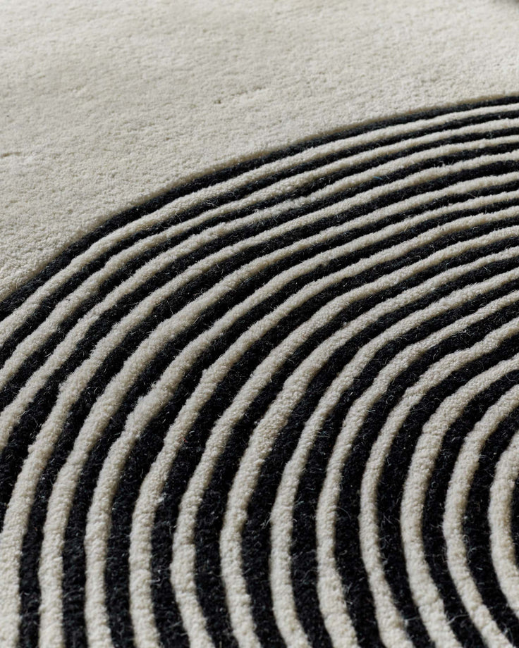 Close-up of sculpted wool rug with curved monochrome striped pattern in cream and charcoal tones.