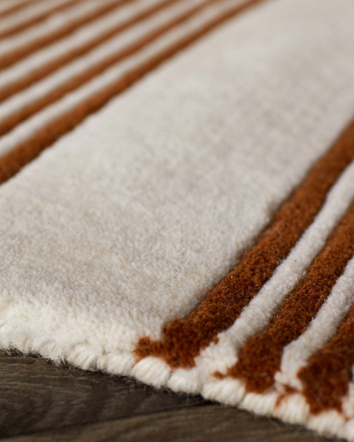 Close-up of rust and cream striped wool rug with sculpted texture and fringe edge detail.