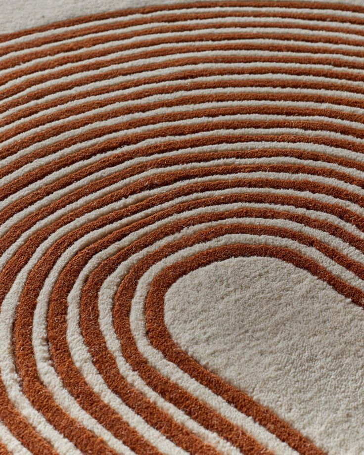Close-up of rust and cream sculpted wool rug with concentric rectangular pattern and textured surface.