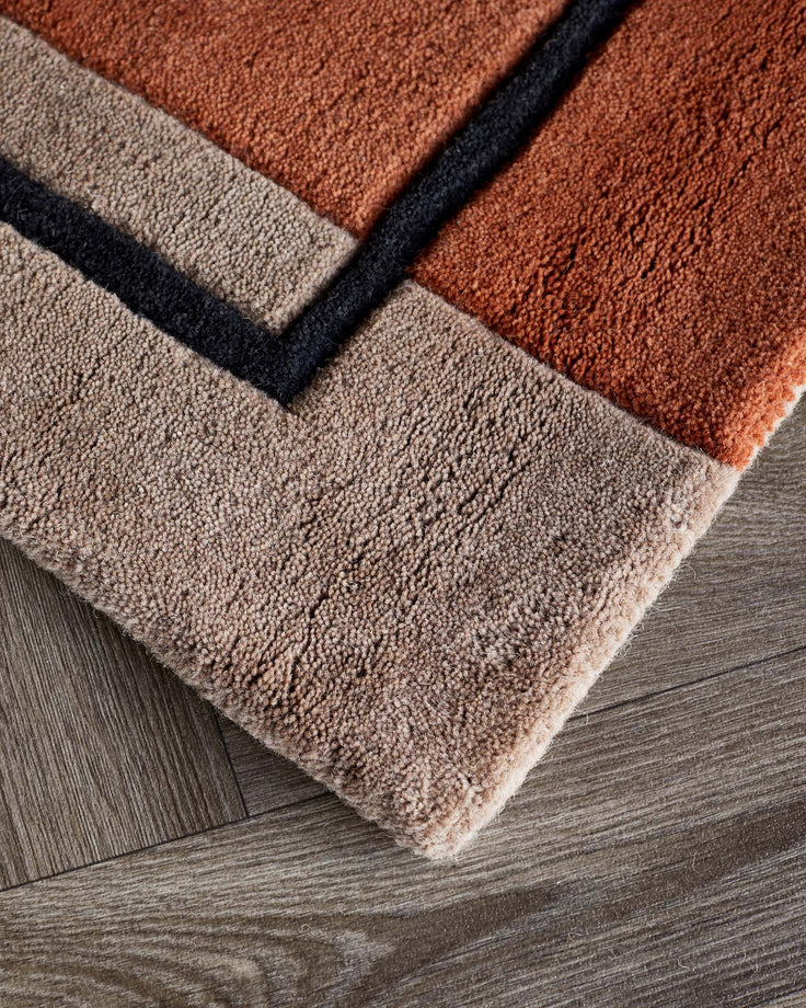 Abstract geometric wool rug with deep red, cream, and black squares on grey wooden floor.