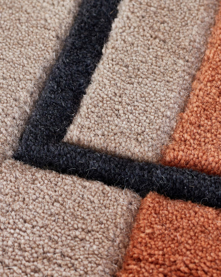 Close-up of abstract wool rug with geometric squares in cream, black, and rust red with sculpted texture detail.
