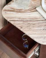 Adalynn bedside table with round travertine marble top and open drawer revealing eyeglasses inside.