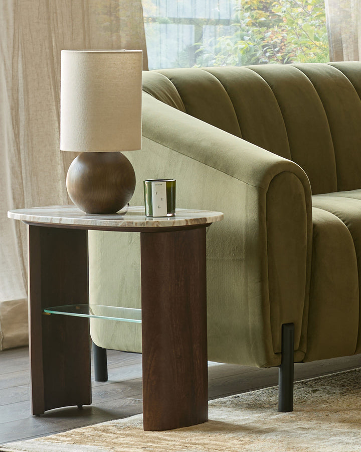 Lamp atop a marble side table next to a stylish, sage green sofa. A sophisticated living room design.